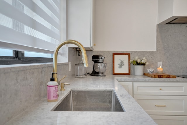 kitchen featuring light stone countertops, tasteful backsplash, extractor fan, sink, and white cabinetry