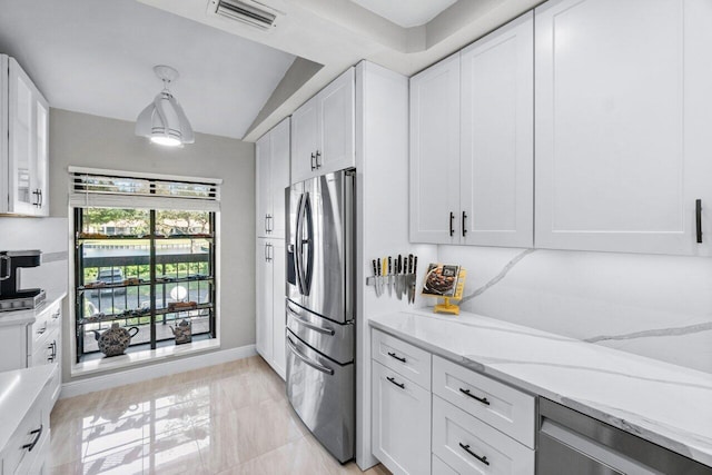 kitchen featuring pendant lighting, lofted ceiling, stainless steel fridge, light stone countertops, and white cabinetry