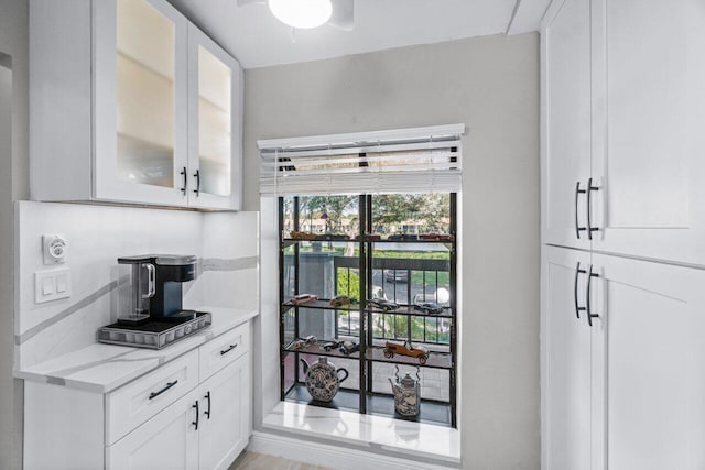 kitchen featuring decorative backsplash, light hardwood / wood-style floors, light stone countertops, and white cabinetry