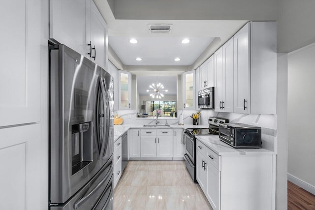 kitchen with sink, stainless steel appliances, a notable chandelier, pendant lighting, and white cabinets