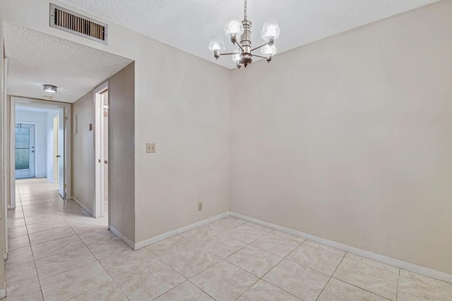 tiled empty room featuring a chandelier and a textured ceiling