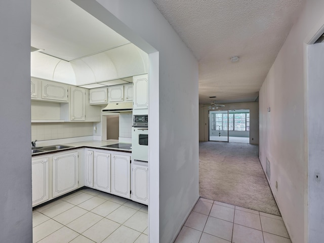 kitchen with sink, white oven, cooktop, a textured ceiling, and light tile patterned flooring