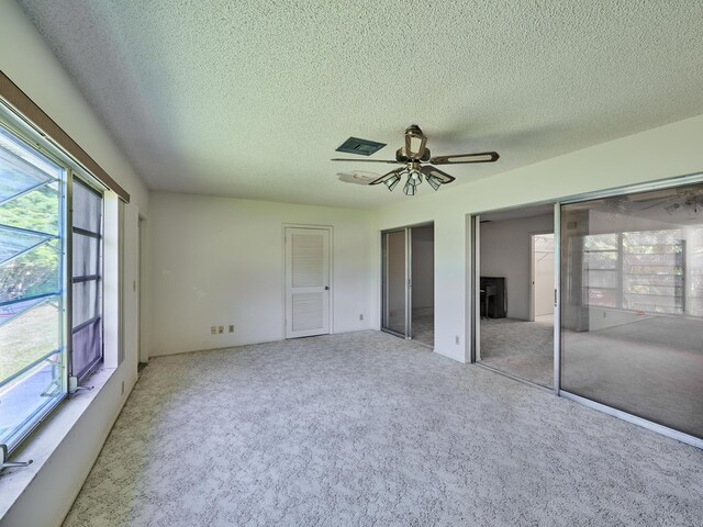 unfurnished bedroom featuring multiple closets, ceiling fan, light carpet, and a textured ceiling