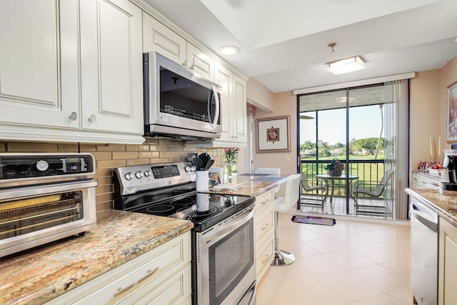 kitchen featuring decorative backsplash, light stone counters, stainless steel appliances, light tile patterned floors, and white cabinets