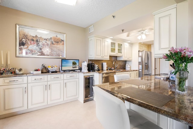 kitchen with a kitchen breakfast bar, a textured ceiling, stainless steel appliances, white cabinetry, and wine cooler