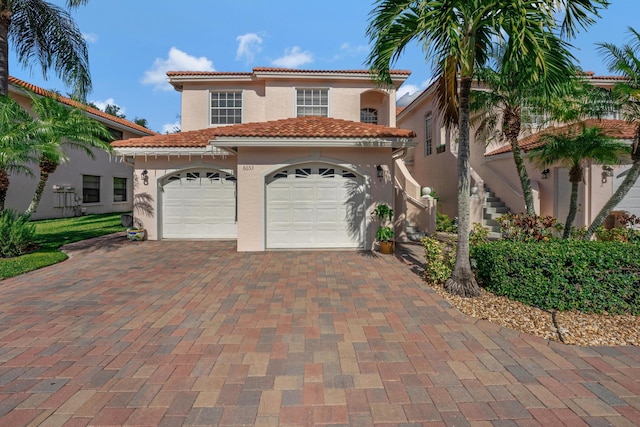 mediterranean / spanish-style home featuring a garage, a tile roof, stairway, decorative driveway, and stucco siding