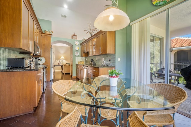 kitchen with appliances with stainless steel finishes, sink, decorative backsplash, dark stone counters, and dark wood-type flooring