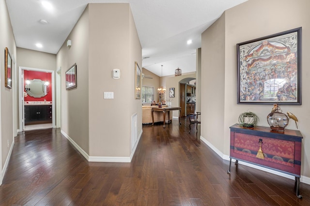 hallway featuring lofted ceiling, wood-type flooring, arched walkways, and baseboards