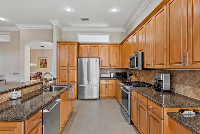 kitchen with sink, stainless steel appliances, ornamental molding, and dark stone countertops