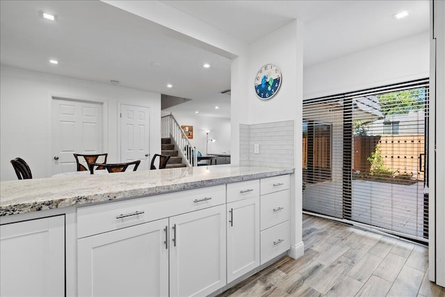 kitchen with white cabinetry, light hardwood / wood-style flooring, and light stone counters