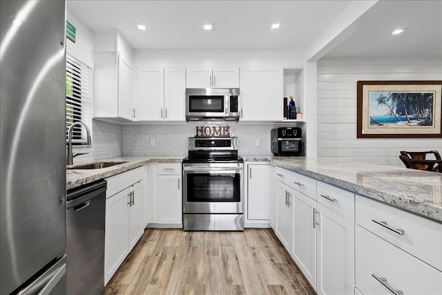 kitchen featuring white cabinetry, sink, light stone counters, light hardwood / wood-style flooring, and appliances with stainless steel finishes