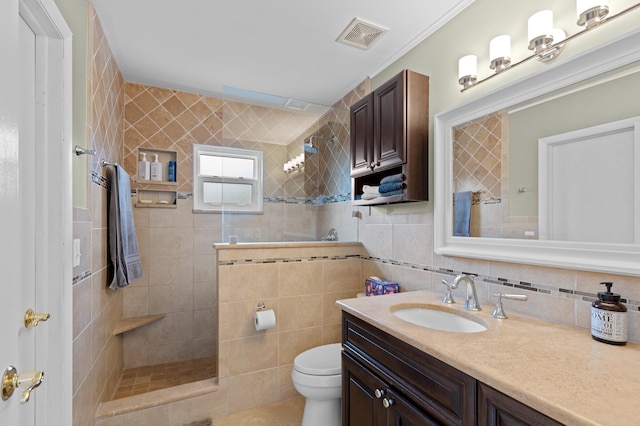 bathroom featuring backsplash, a tile shower, vanity, tile walls, and toilet