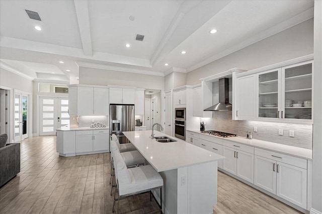 kitchen featuring visible vents, wall chimney range hood, appliances with stainless steel finishes, a kitchen breakfast bar, and a sink