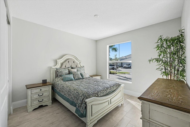 bedroom with a textured ceiling, baseboards, and wood finish floors