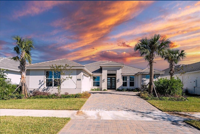 prairie-style home with decorative driveway, a lawn, and stucco siding