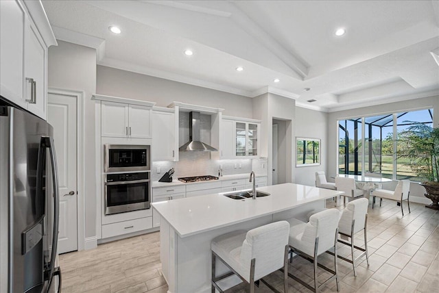 kitchen with a breakfast bar area, a sink, decorative backsplash, appliances with stainless steel finishes, and wall chimney exhaust hood