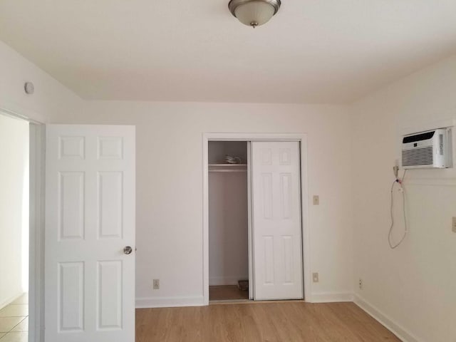 unfurnished bedroom with a wall mounted AC, a closet, and light hardwood / wood-style floors