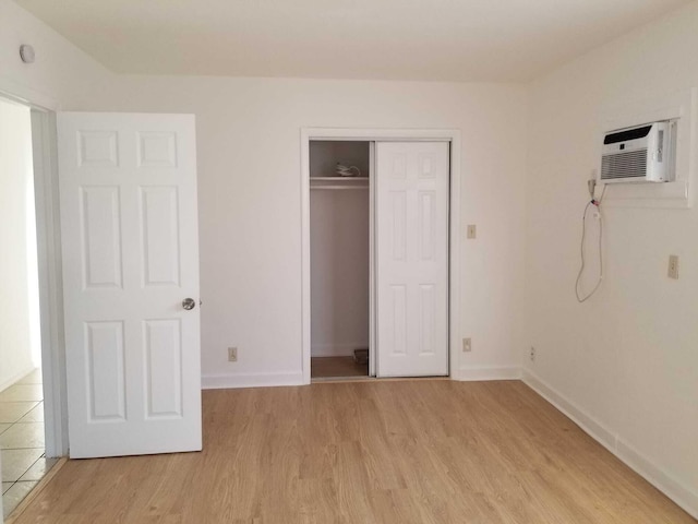 unfurnished bedroom featuring light hardwood / wood-style flooring, a closet, and an AC wall unit