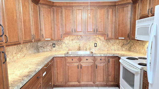 kitchen with a sink, white appliances, light stone counters, and brown cabinetry