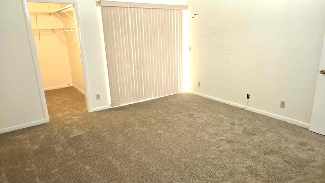 unfurnished bedroom featuring a spacious closet, a closet, and dark carpet