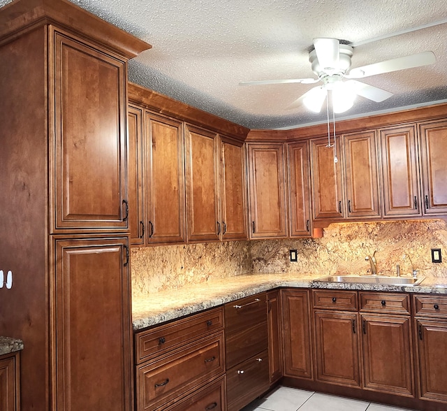 kitchen with light stone countertops, sink, ceiling fan, a textured ceiling, and light tile patterned flooring