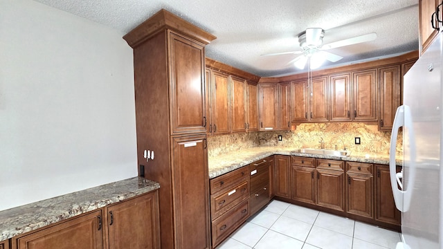 kitchen featuring ceiling fan, sink, light stone countertops, white fridge, and a textured ceiling