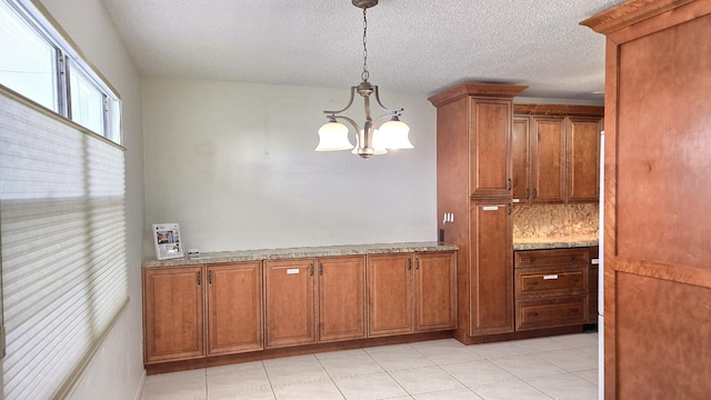 kitchen featuring brown cabinetry, light stone counters, decorative light fixtures, a textured ceiling, and a chandelier