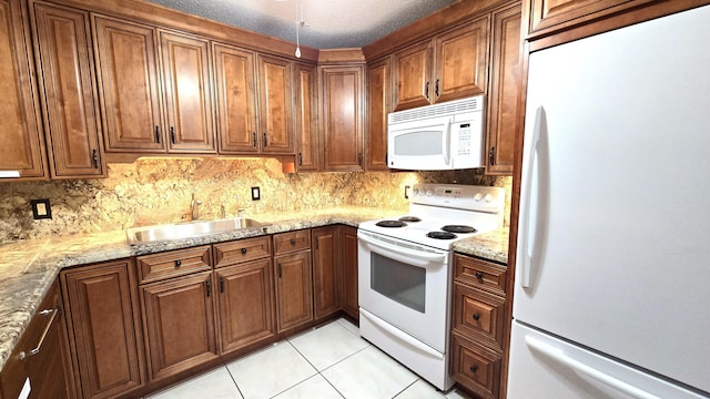 kitchen featuring white appliances, sink, light tile patterned floors, a textured ceiling, and light stone counters