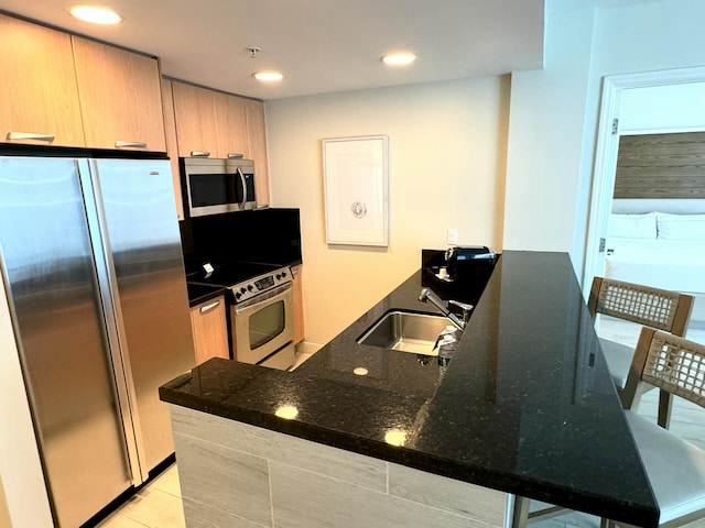 kitchen featuring appliances with stainless steel finishes, dark stone counters, a breakfast bar, sink, and light tile patterned floors