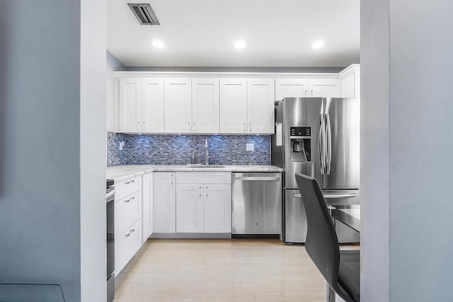 kitchen featuring white cabinets, sink, decorative backsplash, appliances with stainless steel finishes, and light hardwood / wood-style floors