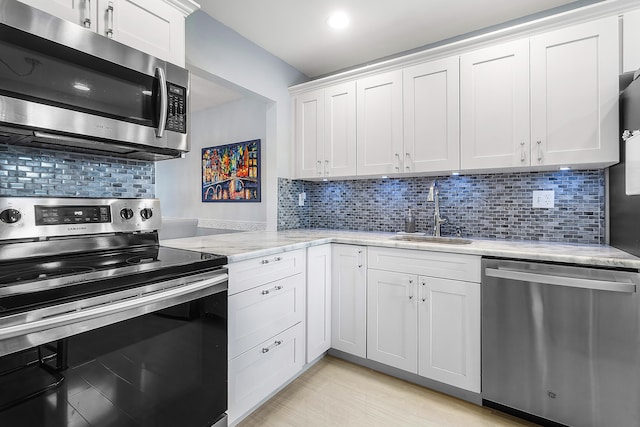 kitchen with stainless steel appliances, white cabinetry, tasteful backsplash, and sink