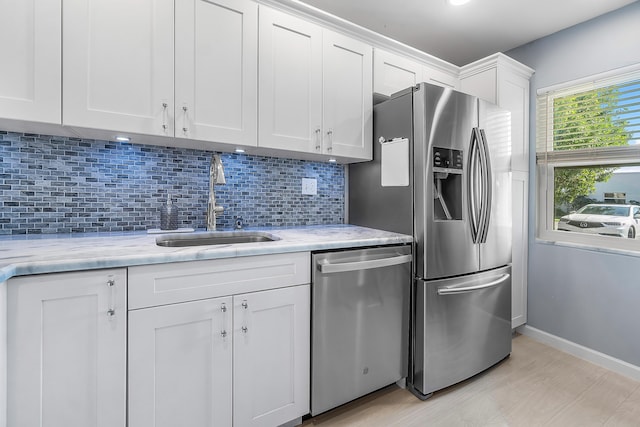 kitchen with light stone countertops, sink, stainless steel appliances, white cabinets, and light wood-type flooring