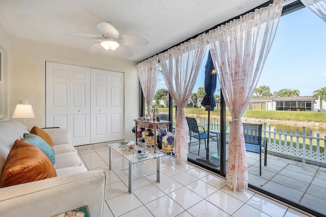 tiled living room featuring a textured ceiling, a water view, and ceiling fan