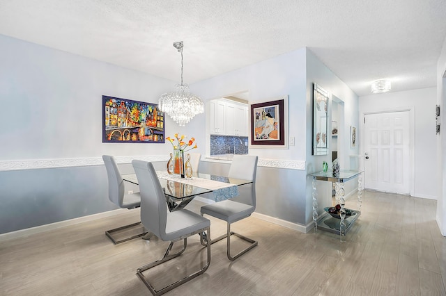 dining space with light wood-type flooring, a textured ceiling, and an inviting chandelier