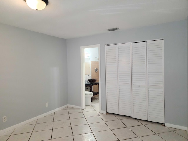 unfurnished bedroom featuring connected bathroom, a closet, and light tile patterned flooring