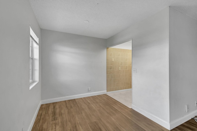 unfurnished room featuring a textured ceiling, tile walls, and light hardwood / wood-style flooring