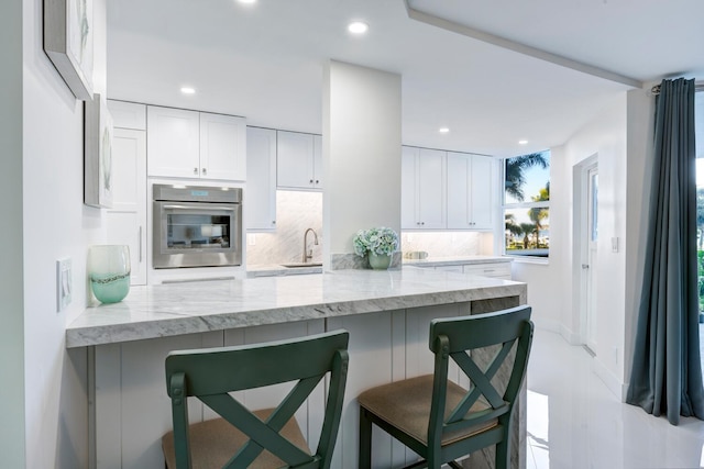 kitchen with kitchen peninsula, a breakfast bar, white cabinets, and oven