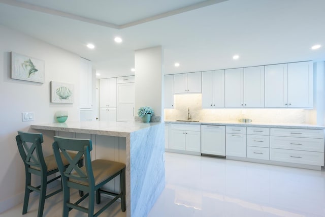 kitchen with kitchen peninsula, a kitchen breakfast bar, tasteful backsplash, dishwasher, and white cabinets