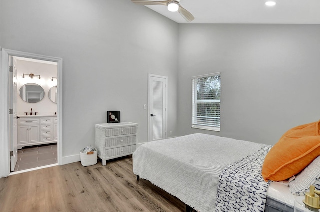 bedroom featuring ensuite bath, a closet, light hardwood / wood-style floors, a towering ceiling, and ceiling fan