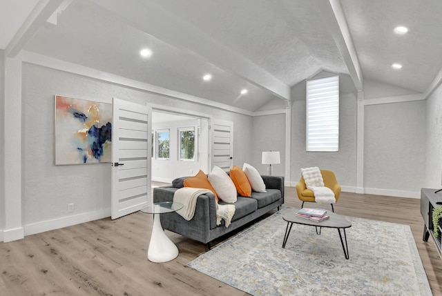 living room featuring vaulted ceiling with beams, plenty of natural light, light wood-style flooring, and baseboards