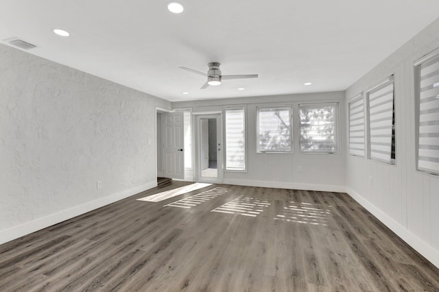 empty room featuring visible vents, a textured wall, dark wood-type flooring, a ceiling fan, and baseboards