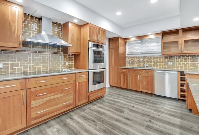 kitchen with stainless steel appliances, wall chimney range hood, tasteful backsplash, and light hardwood / wood-style flooring