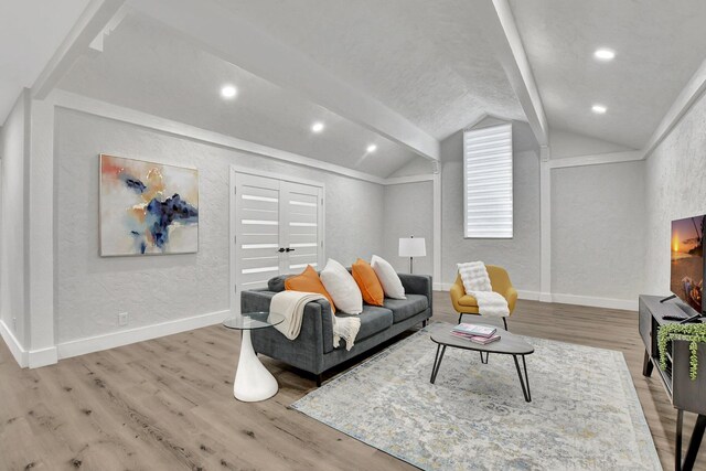 living area with vaulted ceiling with beams, a textured wall, light wood-style flooring, and baseboards