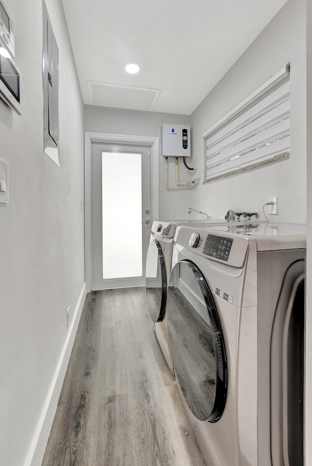 clothes washing area featuring laundry area, electric panel, baseboards, wood finished floors, and washing machine and dryer