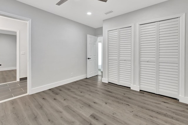 unfurnished bedroom with wood finished floors, visible vents, a ceiling fan, baseboards, and two closets