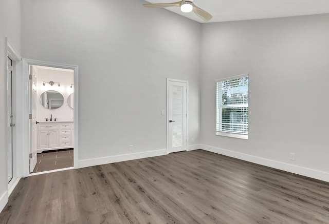 unfurnished bedroom with a closet, ensuite bath, ceiling fan, dark wood-type flooring, and a high ceiling