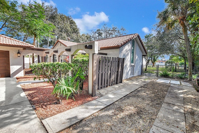 view of property exterior with a gate, fence, a tiled roof, and stucco siding