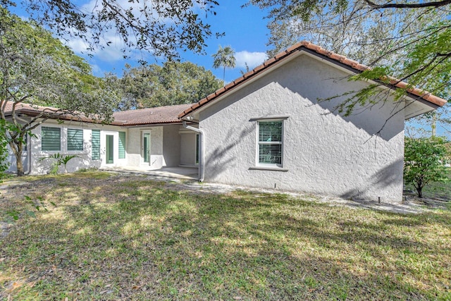 back of house featuring a yard, a tile roof, and stucco siding