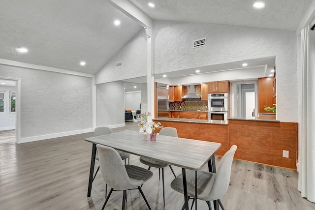 dining space featuring beam ceiling, light hardwood / wood-style floors, and high vaulted ceiling