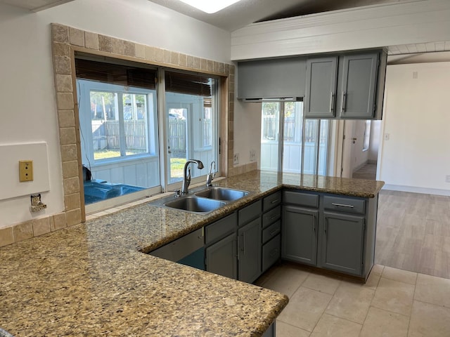 kitchen featuring gray cabinetry, kitchen peninsula, sink, and stone counters